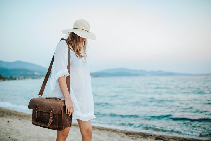 年輕女子帶著棕色袋子在海灘上行走，海灘